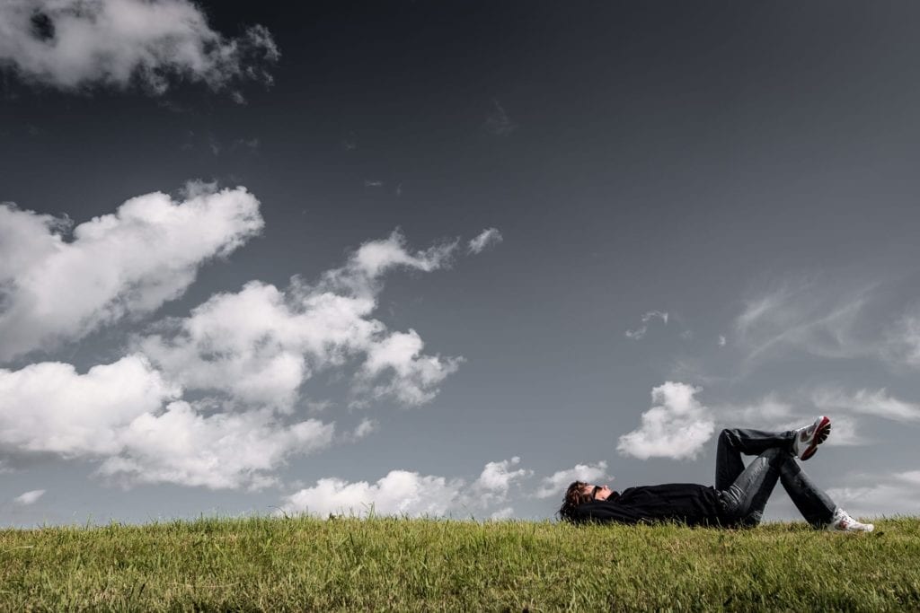 Mann som ligg i graset og kikar opp på himmelen